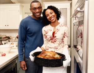 Portrait of a Couple Standing Side by Side in a Kitchen, with the Woman Proudly Holding a Roasting Dish Containing a Cooked Turkey